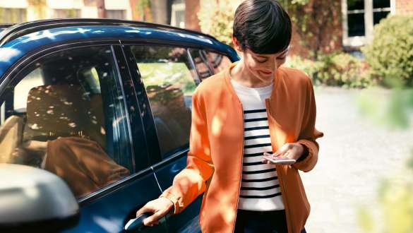Woman looks at her smartphone and opens the door of her BMW BMW Teleservices Woman looks at her smartphone and opens the door of her BMW