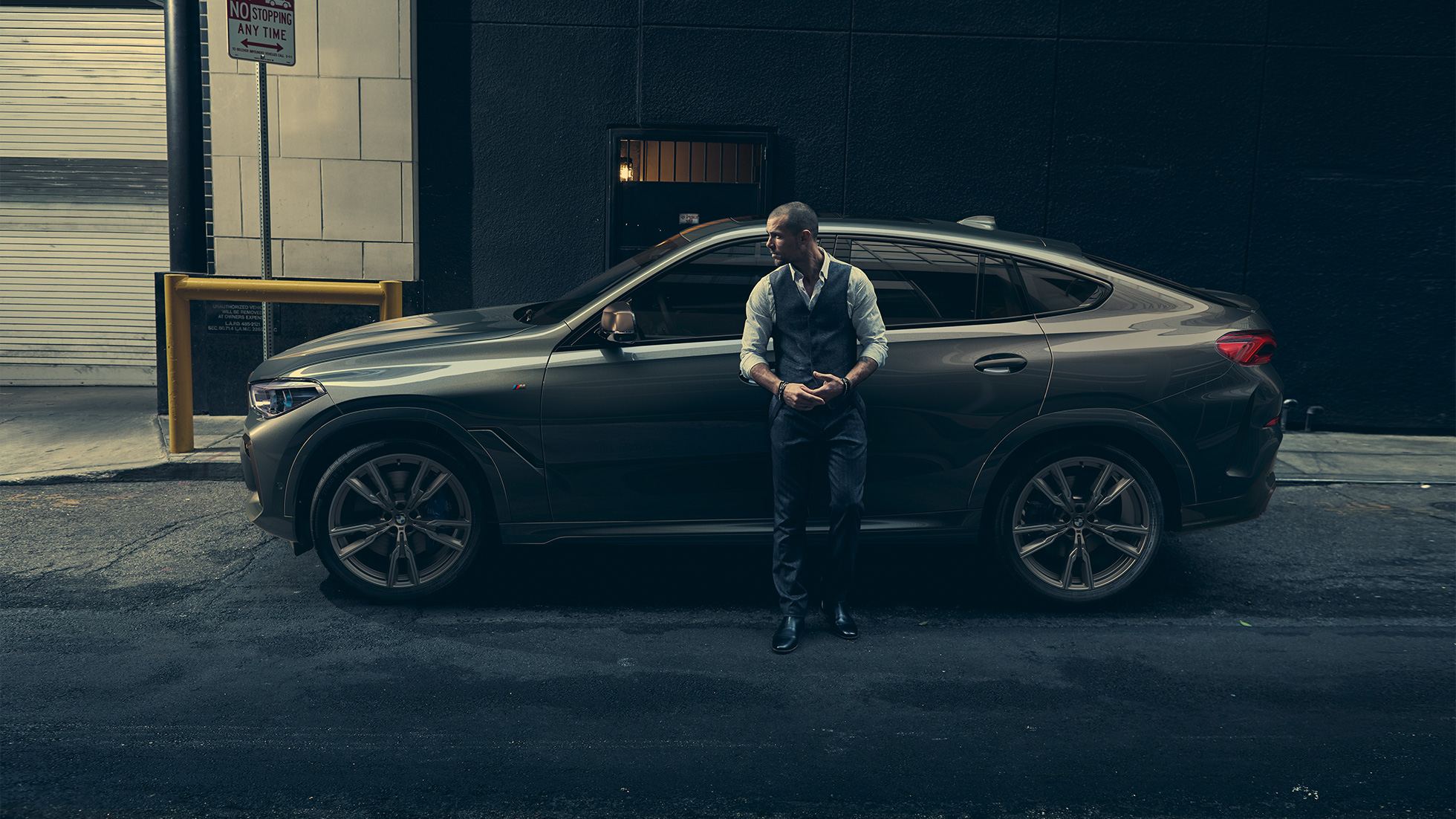 BMW X6 M50i in lateral perspective. Man leaning on BMW X6 M50i in lateral perspective in front of an urban setting.