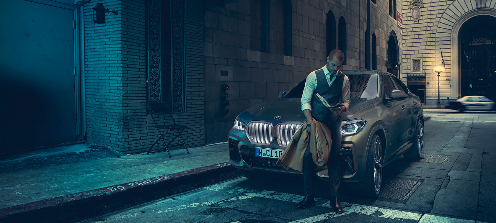 Front of BMW X6 M50i. Man leaning on front of the BMW X6 M50i.
