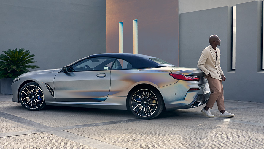 BMW M850i xDrive Convertible G14 LCI Facelift 2022 BMW Individual Frozen Pure Grey metallic three-quarter rear view with male model leaning against vehicle