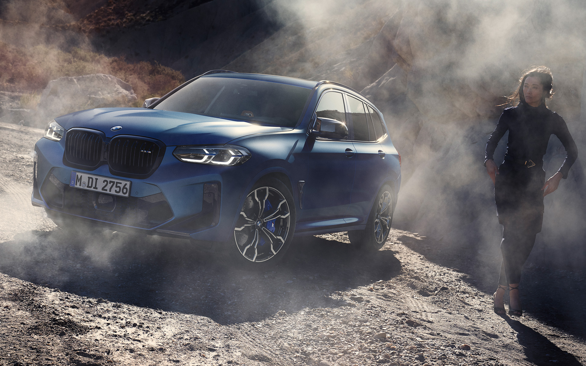 BMW X3 M Competition F97 LCI Facelift 2021 Frozen Marina Bay Blue metallic three-quarter front view standing in stony terrain with female model
