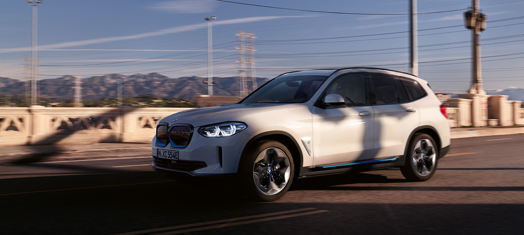 BMW iX3 G08 three-quarter front view driving on road BMW iX3 G08 2020 Mineral White metallic three-quarter front view driving on road