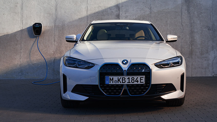 BMW iX xDrive50 i20 three-quarter rear view in the garage next to high-voltage socket and charging cable hanger