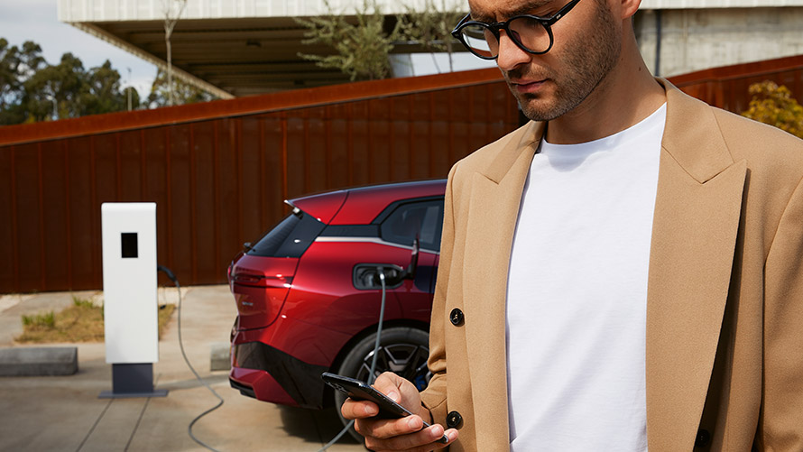 Man with smartphone in front of BMW iX at charging station