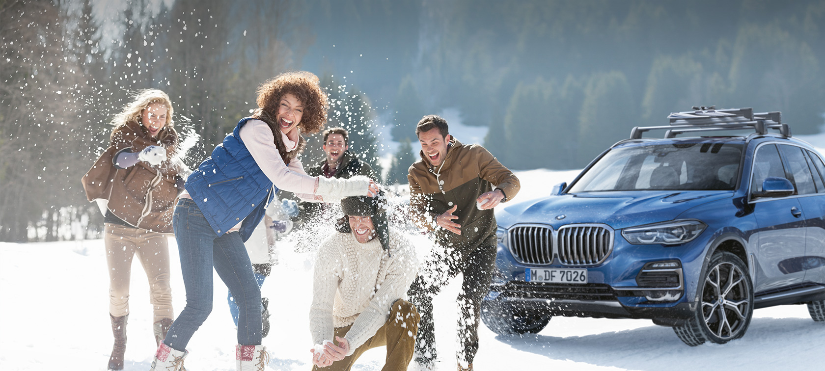 Original BMW Accessories and BMW Service for autumn and winter Women and men laughing in the snow in front of a BMW
